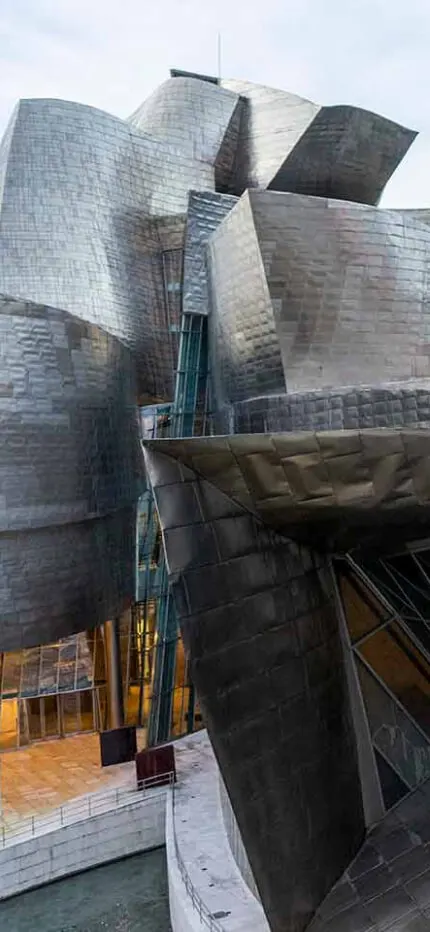 Curving, shimmering titanium walls and angled glass of the Guggenheim Museum Bilbao at dusk.