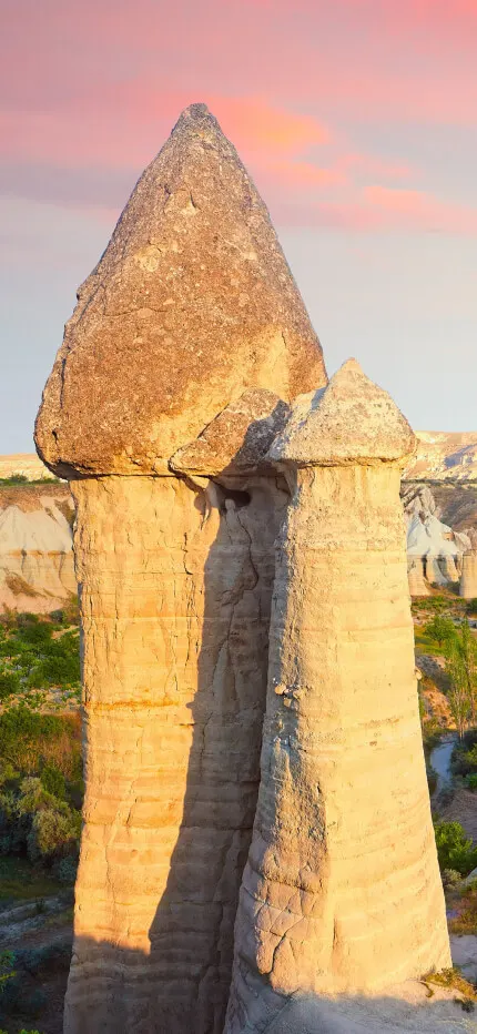 Tall capped rock pinnacles rise above an eroded valley of pale stone formations at sunset.