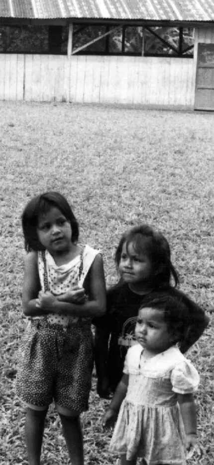 Black-and-white photo of four young children standing barefoot on a grassy clearing.