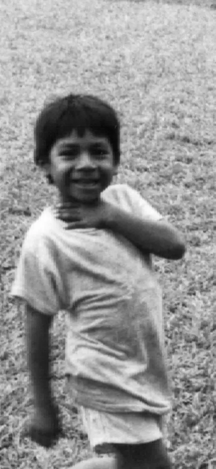 Black-and-white photo of a smiling young boy on a grassy field, hand at his chest.