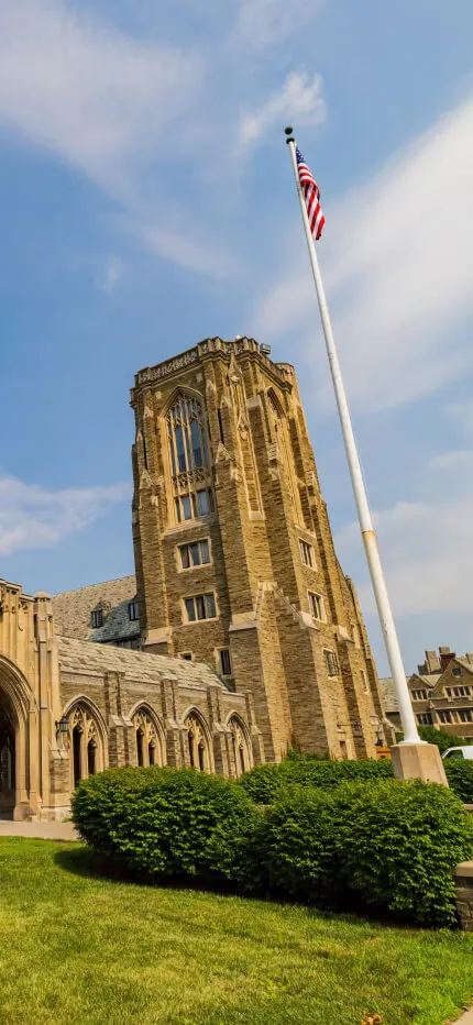 Gothic stone chapel with a tall bell tower, arched cloister windows, and an American flag.