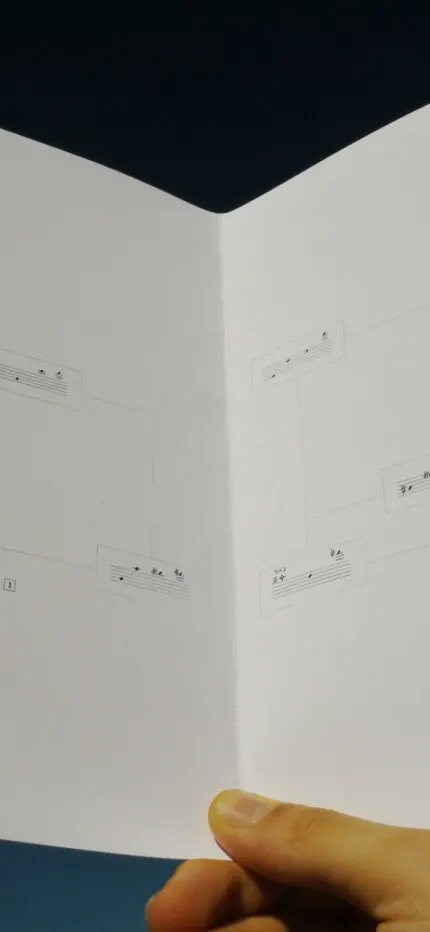 Hand holding open a booklet of short musical staff fragments connected by lines like a map.