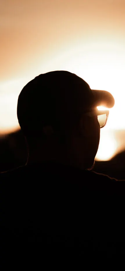 Silhouette of a person in a cap and glasses against a glowing golden sunset
