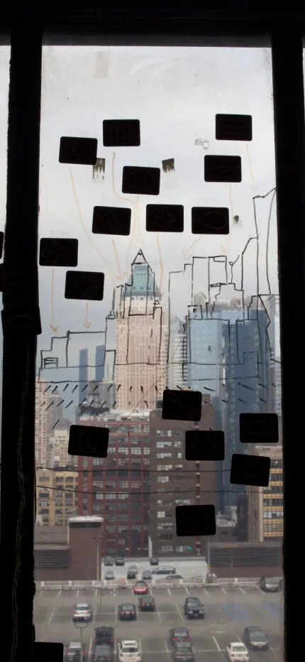 Office window covered in black sticky notes and a hand-drawn skyline over city towers